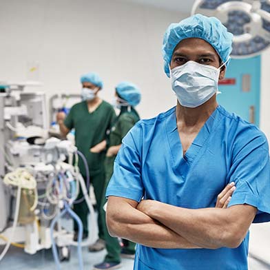 A confident nurse in blue scrubs and a surgical cap stands with arms crossed in an operating room, with medical equipment and colleagues working in the background. A confident nurse in blue scrubs and a surgical cap stands with arms crossed in an operating room, with medical equipment and colleagues working in the background.